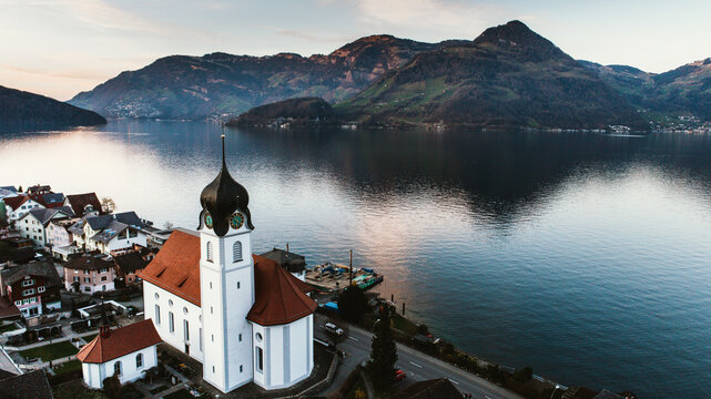 Aerial view of the tranquil Lake Lucerne in Switzerland. Image features a traditional catholic swiss church that overlooks the nearby mountain ranges.