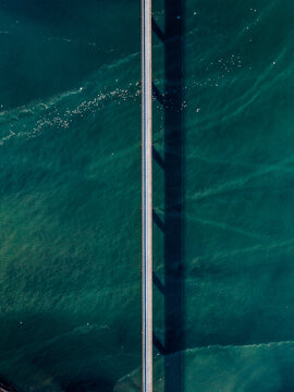 Aerial view of a straight road going over the beautiful blue Atlantic Ocean, surrounded by tiny ice shards in Eyrarbakki, South Iceland