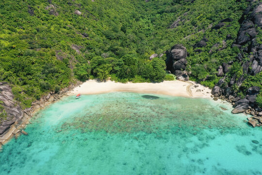 Aerial view of Anse di riz, Mah&Egrave;, Seychelles. A boat drops tourists off at the beach, oblivious to the huge school of fish further down the shore.