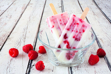 Homemade raspberry vanilla yogurt ice pops. Side view close up in bowl against a white wood...