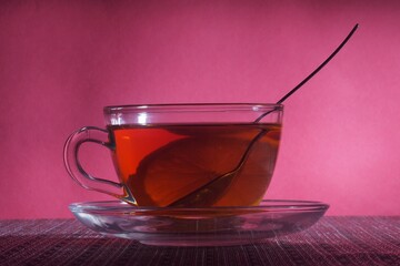 Tea with lemon in a clear glass glass and with a metal teaspoon.