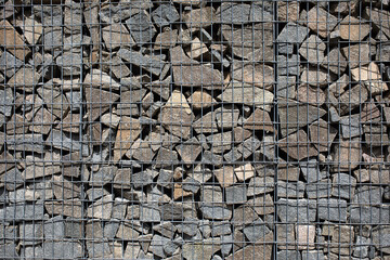 a fragment of a fence made of gray and brown stone and metal mesh for the background or texture.