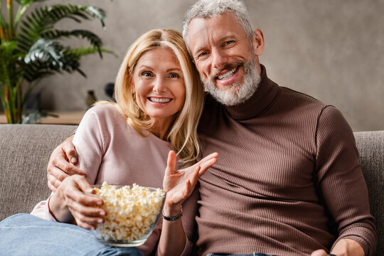 Happy Middle Aged Couple, Wife And Husband Watching Tv And Eating Popcorn