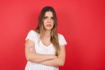 Waist-up portrait of beautiful girl frowning her face in displeasure, wearing casual clothes, keeping arms folded, waiting for an explanation. Attractive young woman in closed posture.