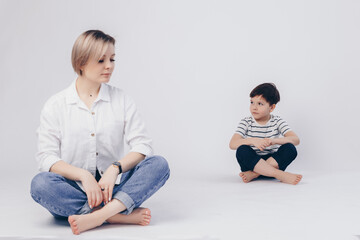 Obraz premium White background. Mom sits in the lotus position in front, her son sits behind as well.