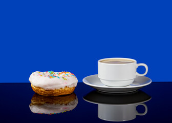 Tasty donut and white cup of coffee with coffee on a blue background with reflection