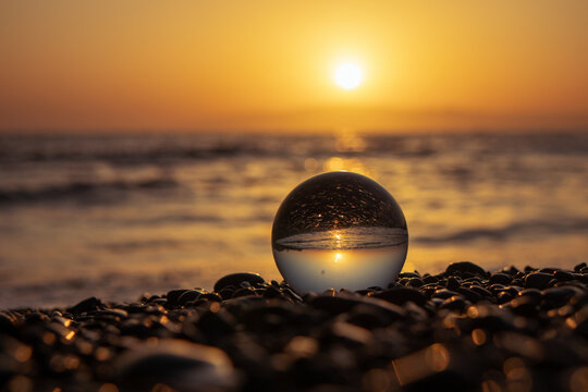 Stones on the ocean shore and waves and splash is reflected in a crystal ball at sunset