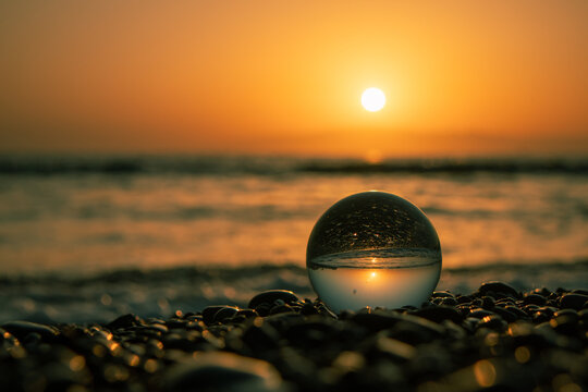 Stones on the ocean shore and waves and splash is reflected in a crystal ball at sunset