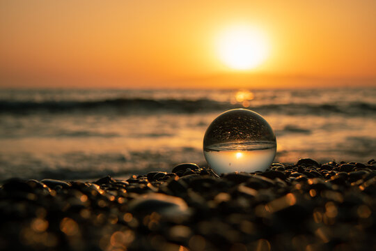 Stones on the ocean shore and waves and splash is reflected in a crystal ball at sunset