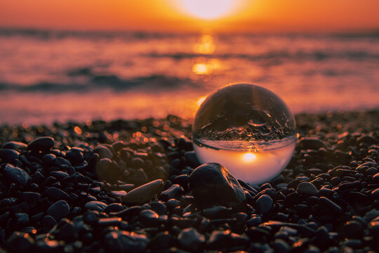 Stones on the ocean shore and waves and splash is reflected in a crystal ball at sunset