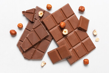 Bar and pieces of milk chocolate, hazelnut on white background flat lay top view copy space. Minimalistic Chocolate Background. Chocolate, cocoa, sweet treat, sugar, overweight, chocolate addiction