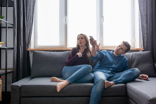 woman sitting on sofa near man holding remote controller from air conditioner while feeling hot
