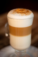Café capuchino con canela en la espuma sobre una mesa de madera.