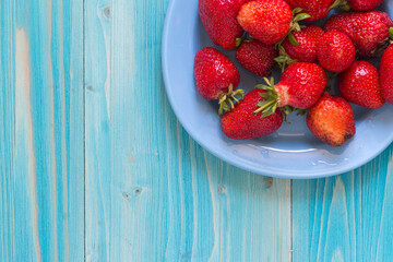 A portion of fresh ripe strawberries in a plate on a blue wooden table. Copy space