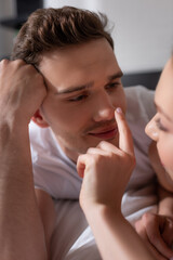 selective focus of girl touching nose of handsome boyfriend in bedroom