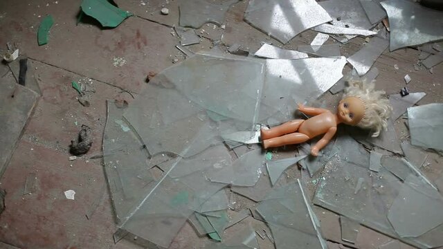 Broken window glass and a childish doll lie on the floor in an abandoned house.