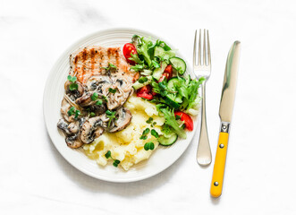 Pork chops, potato mash, creamy mushroom sauce and fresh vegetable salad on a light background, top view