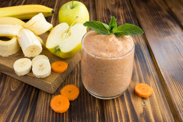 Obraz na płótnie Canvas Smoothies or puree with banana, apple, carrot and ingredients on the brown wooden background