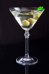 Martini with green olives in a glass on a black  background, location vertical