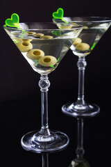Martini with green olives in two glasses  on a black background, location vertical