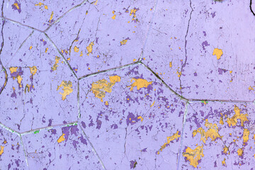 Flaking purple and yellow paint on old wall surface. Building facade with damaged paint. Abstract background, close-up, texture.