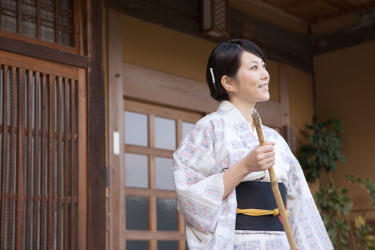 玄関先を箒で掃く和服姿の30代女性