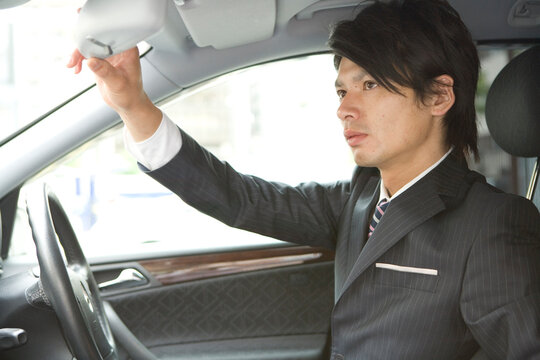 自動車のバックミラーの位置を調整するビジネスマン
