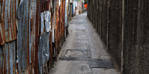 Old corrugated galvanized iron sheet and grunge rough concrete wall on the narrow pathway street,...