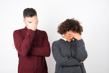 Indoor portrait of beautiful woman with stylish haircut, wearing casual clothes, making facepalm gesture while smiling, standing over gray background amazed with stupid situation.