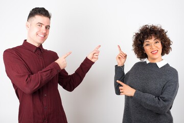 Advertisement concept. Positive, pretty, caucasion woman with beaming smile in jeans shirt on grey background is pointing with her two index finger and looking on empty copy space.