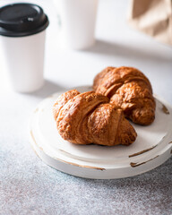 fresh croissants on a light background, in the background coffee in a paper cup