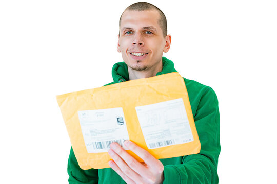 Young man with small beard in green sweatshirt gives an envelope mail to the camera isolated on a white background. Blurred post parcel for documents with labels. Delivering. Shipping. Package. Postal