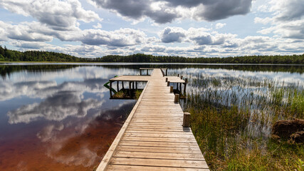 Landscape with a swamp lake and with a wooden footbridge. Beautiful clouds and the surrounding forest were reflected in dark water. Latvia. Lake Ratnieku