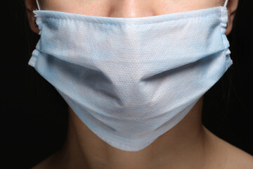 Young woman wearing face medical mask to prevent infection, illness or flu and 2019-nCoV. Black background. Protection against disease, coronavirus.