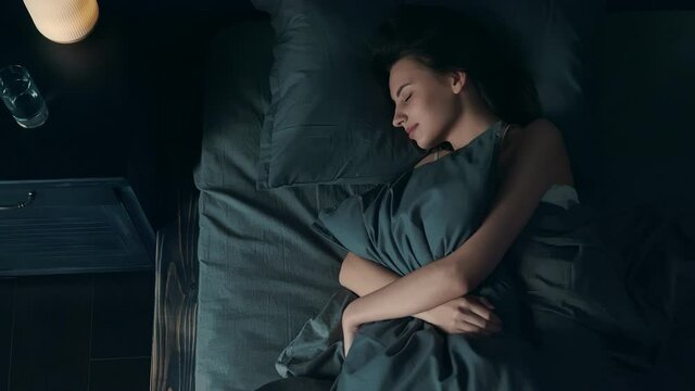 Top View of Beautiful Young Woman Sleeping Cozily in Bed. Girl Hugging a Pillow while Lying in Bed. Loft Bedroom Interior.