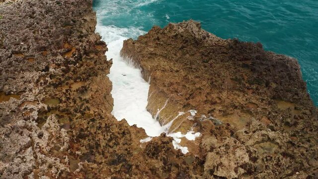 Aerial view of ocean waves beat into cracks in the rocks and a powerful jet of water breaks out of them. Danger water blow. Sea waves and water crashing on a rocky beach aerial view drone shot.