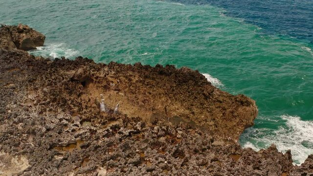 Aerial view of ocean waves beat into cracks in the rocks and a powerful jet of water breaks out of them. Danger water blow. Sea waves and water crashing on a rocky beach aerial view drone shot.