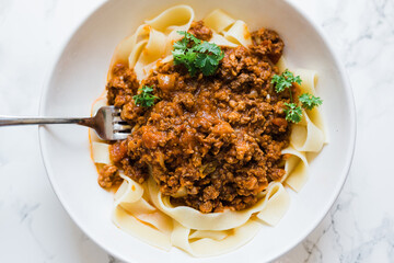 A beautiful plated bowl with fork of linguini noodles with bolognese sauce. Sprigs of green parsley are on top. Horizontal Photo, Close-up food photography.