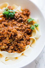 A vertical close up of spaghetti sauce over noodles on a white bowl with sprigs of parsley. This is a delicious Italian dish.