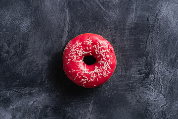 Pink donut with sprinkles, sweet glazed dessert food on dark concrete textured background, top view