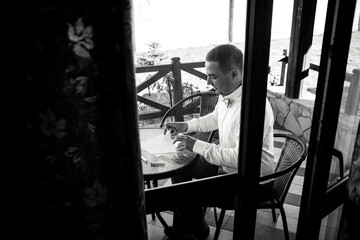 Obraz premium Black and white photo the groom in a shirt sits at a table on the terrace and writes a letter to the bride