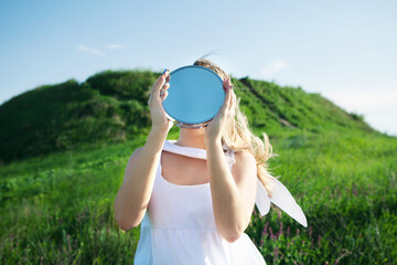 Woman holds mirror with sky reflection instead of head. Concept unity with nature, despair, loneliness, nostalgia, memories.