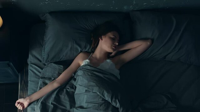 Young Beautiful Woman Sleeping in Cozy Bed. Girl Moving Arms and Stretching while Falling Asleep. Young Woman Sleeping Badly.