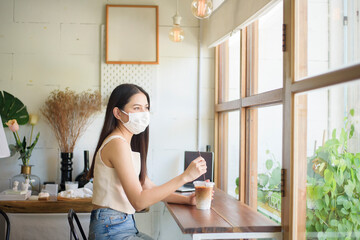 Fototapeta na wymiar Beautiful young Woman with face mask is sitting in coffee shop