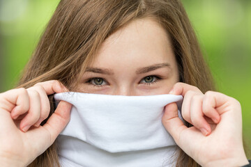 Expressive eyes of a young girl, brunette. The wide collar of her white sweater covers her face. On a green background.