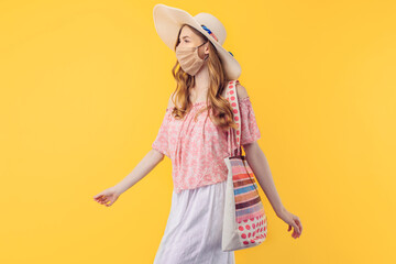 young woman in a summer hat, wearing a protective medical mask against the virus, on an yellow background