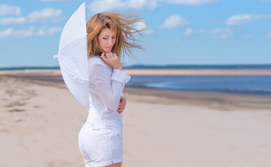 Red-haired woman stands on the beach in white clothes with a white umbrella in her hands on the background of the sea