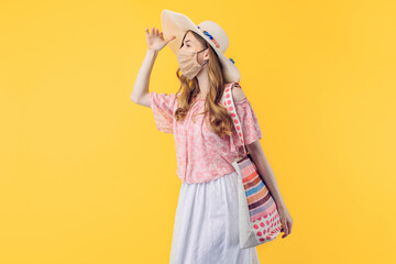 young woman in a summer hat, wearing a protective medical mask against the virus, looks into the distance on an yellow background