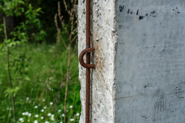 Concrete light gray pillar close-up, with rusty iron wire (lightning conduit) passing along its dyna against the background of forest and green grass.