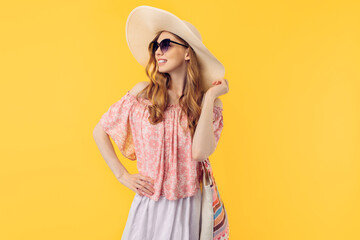 Happy young attractive woman in a summer hat and sunglasses, on an yellow background